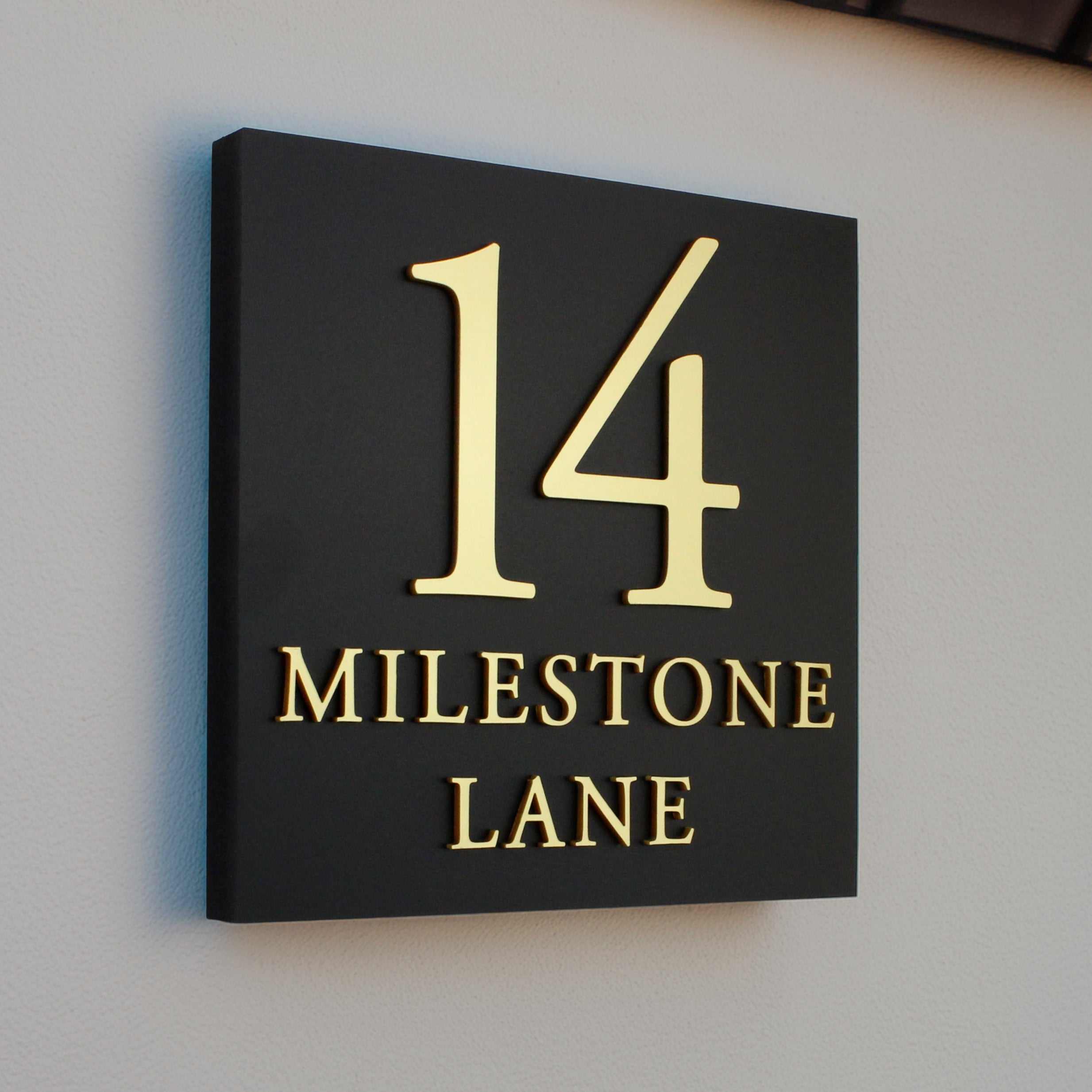 square Black sign with gold text in a raised design large number and 2 lines of text