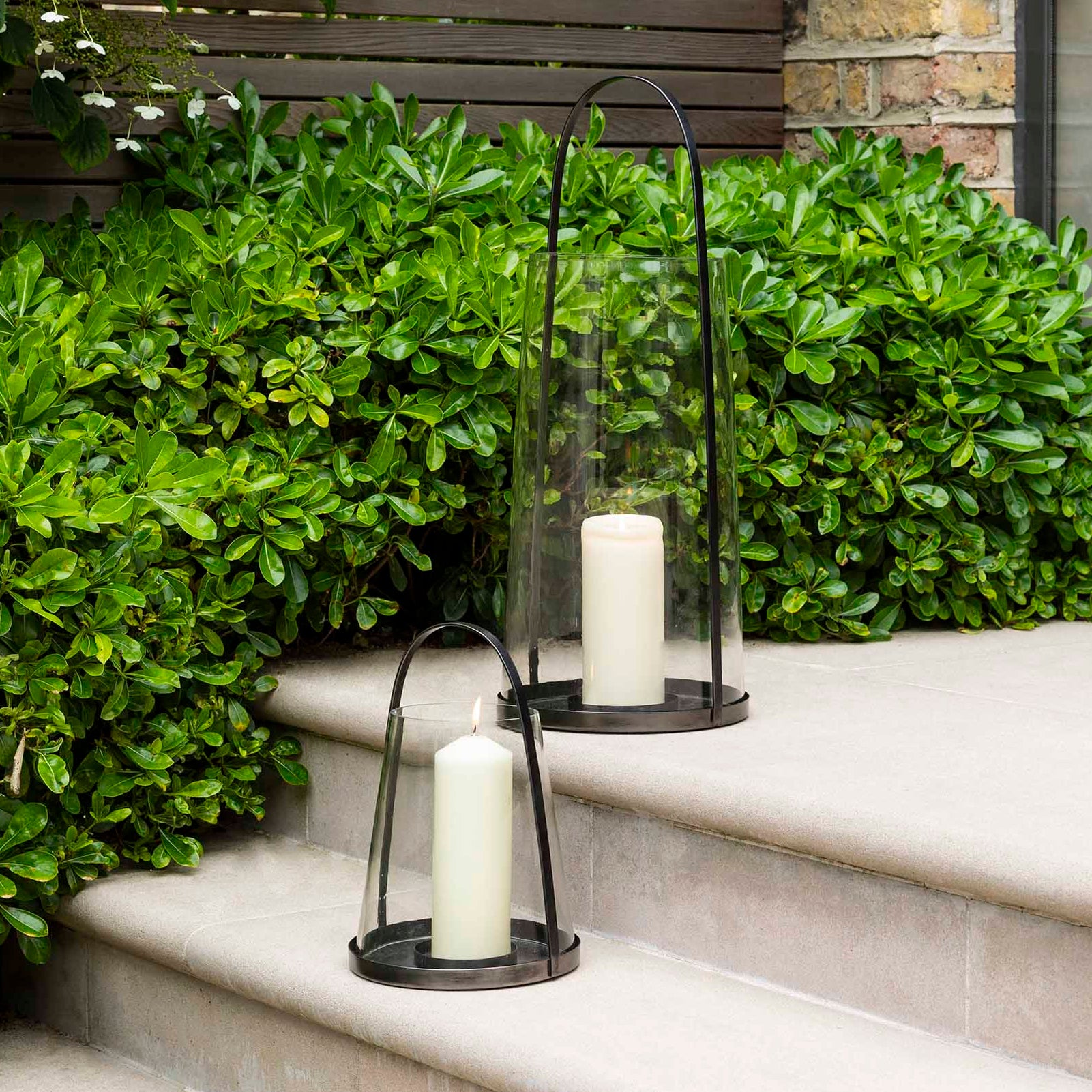 Candle lanterns on outdoor steps with greenery in the background