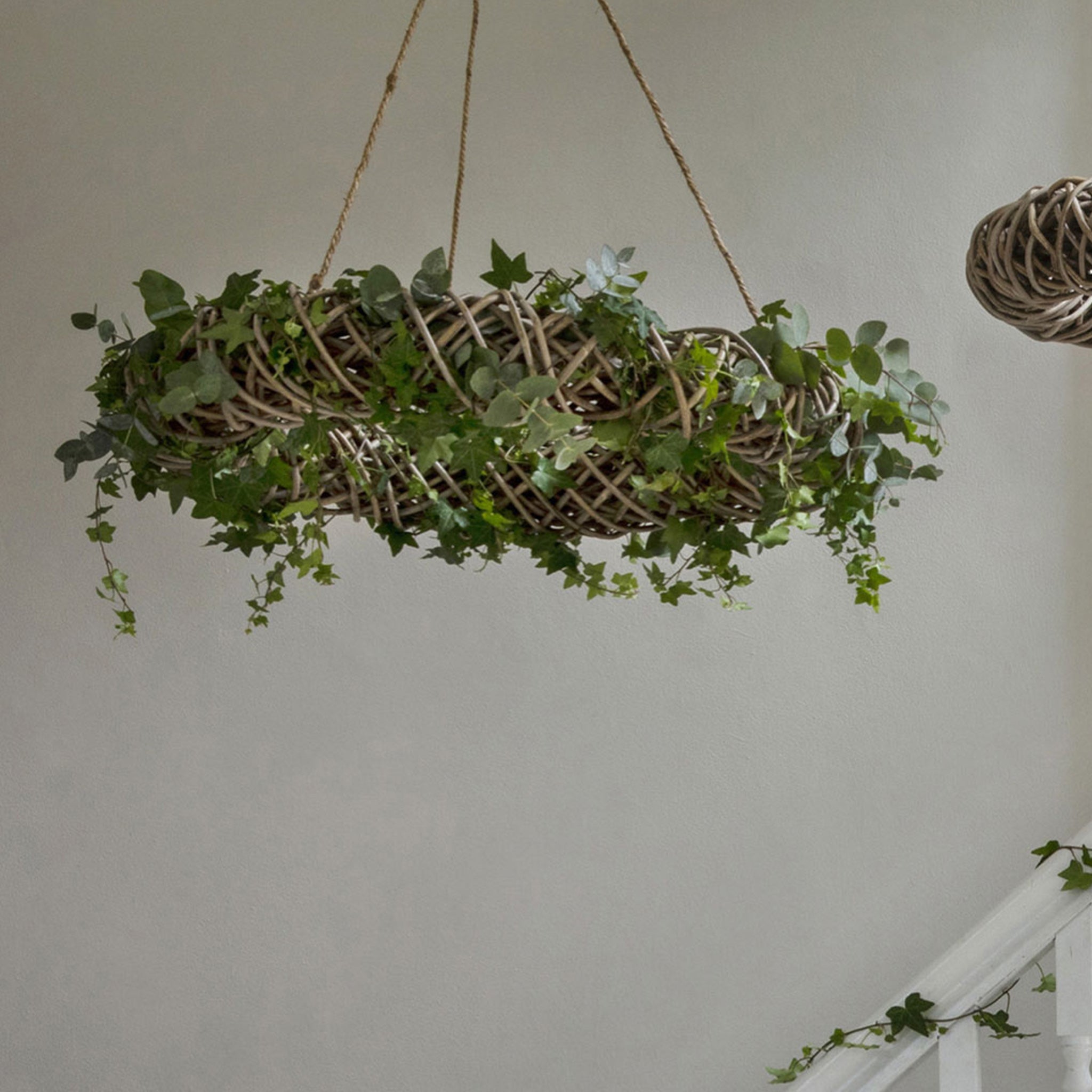 A natural brown hanging wreath base with greenery starts to fill the frame, hanging by ropes, intended for decorative purposes.