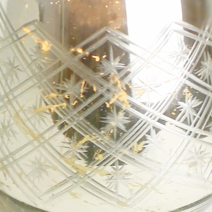 "Close-up of a glass candle holder featuring intricate silver and gold foil, perfect for creating a warm, inviting ambiance."