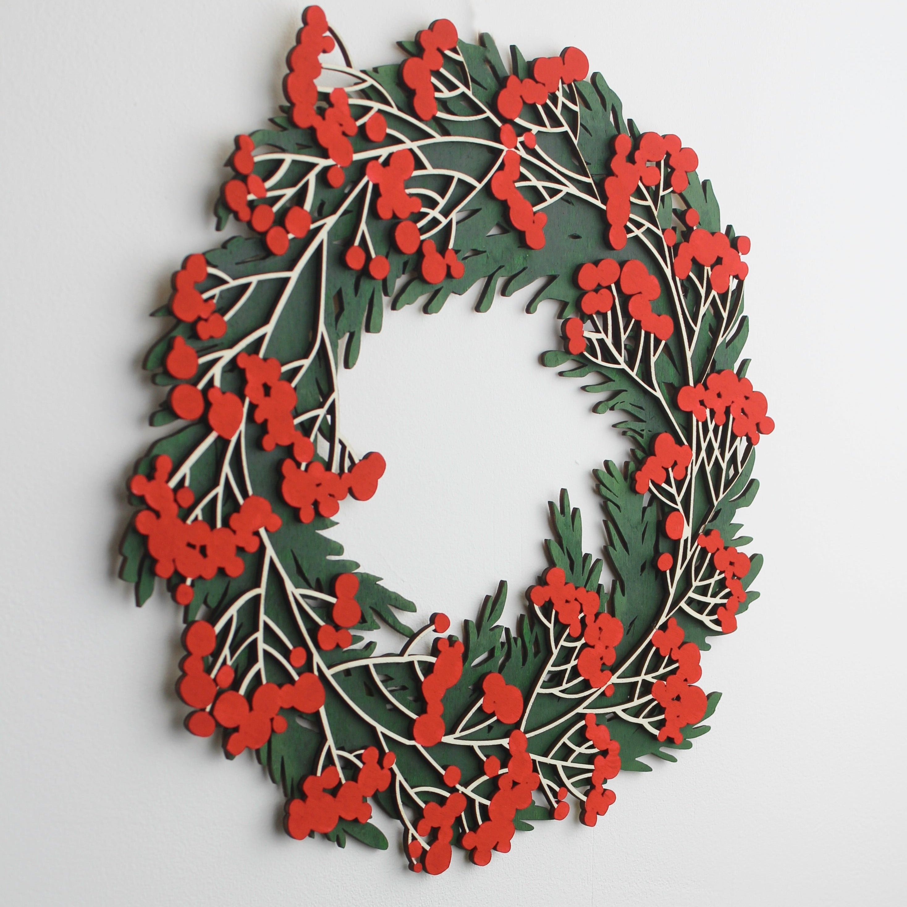 A hand-painted wooden wreath with deep greens and rich red berries, designed to resemble a winter holiday decoration.