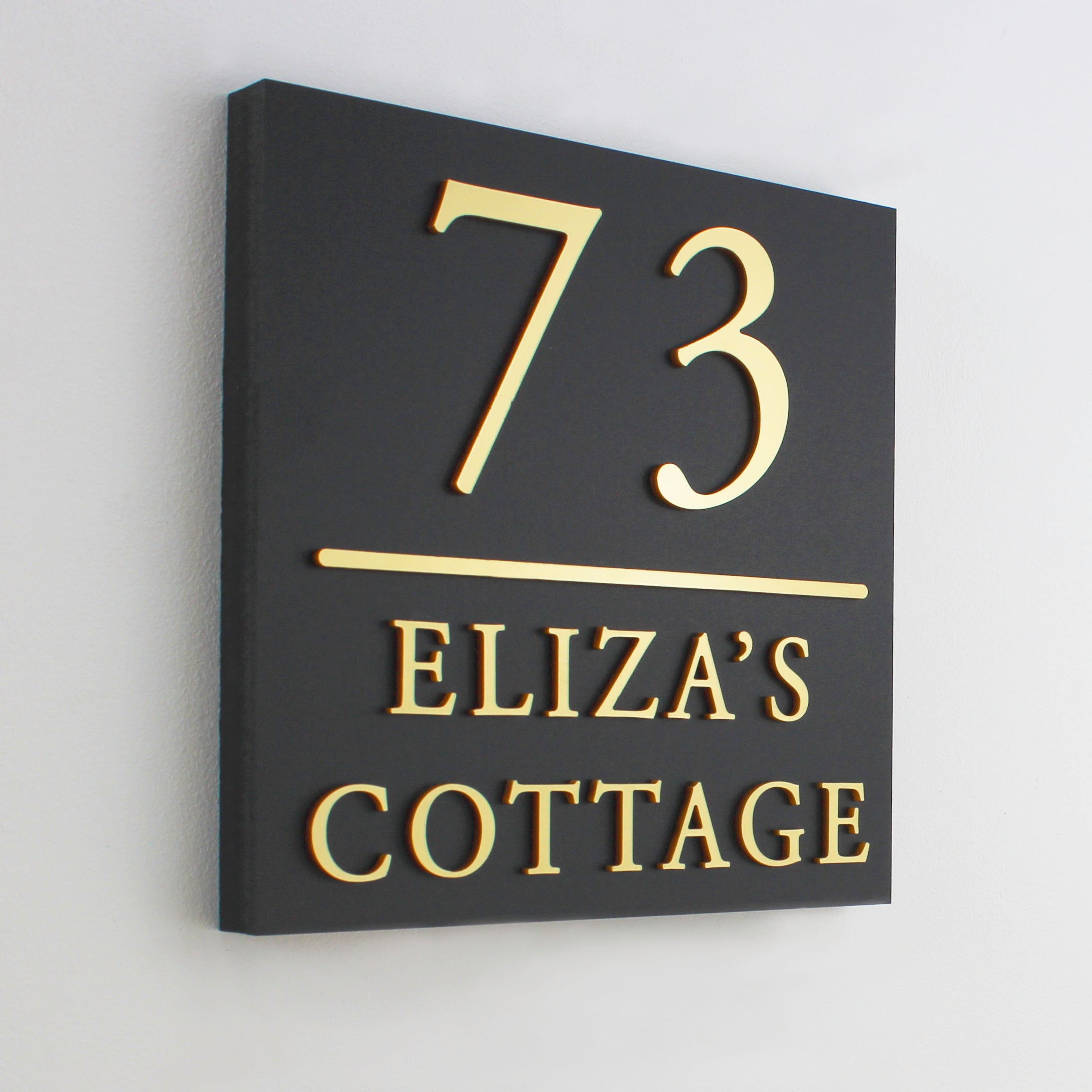 square matte black house sign with dividing line shown in gold