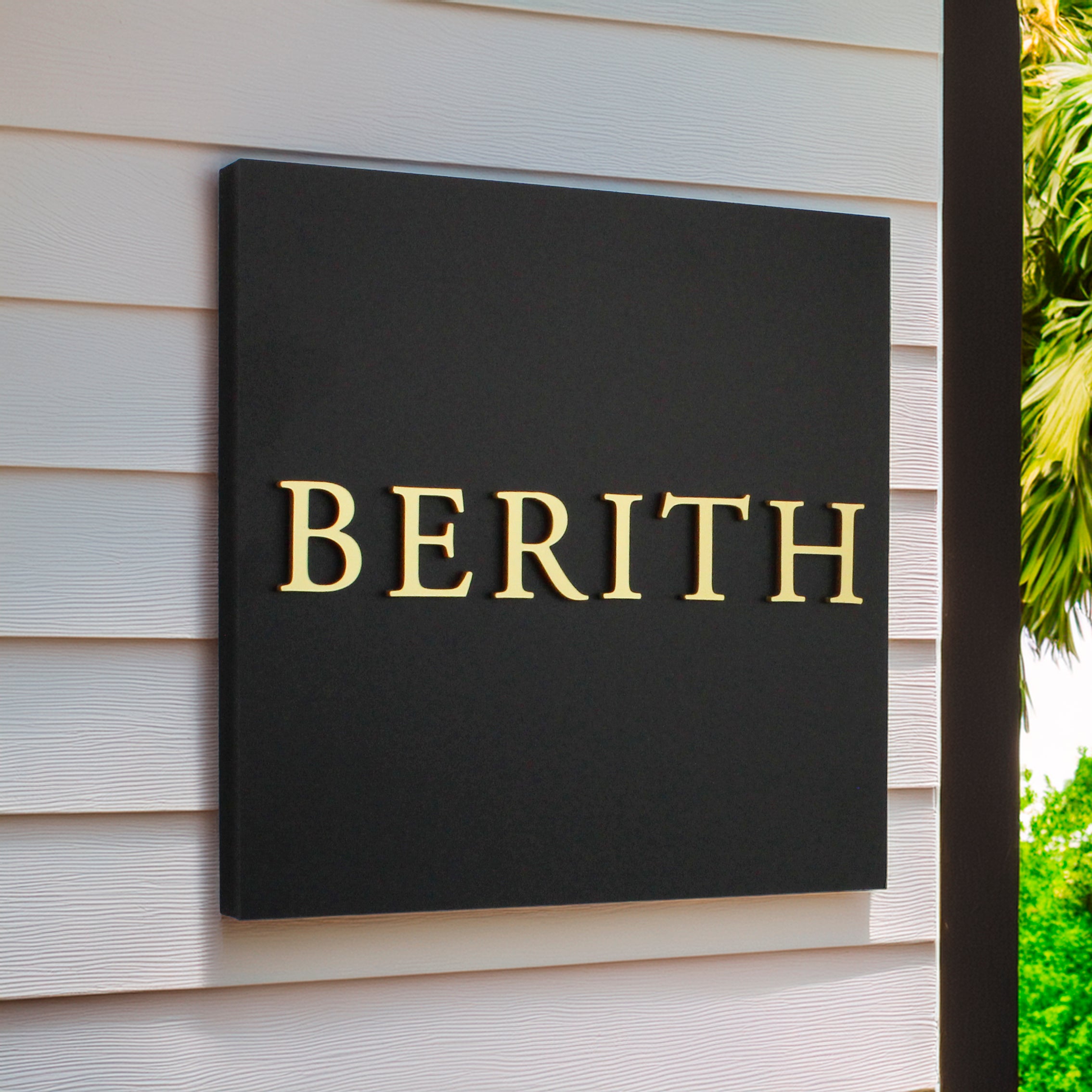 Black sign with square shape with raised gold lettering