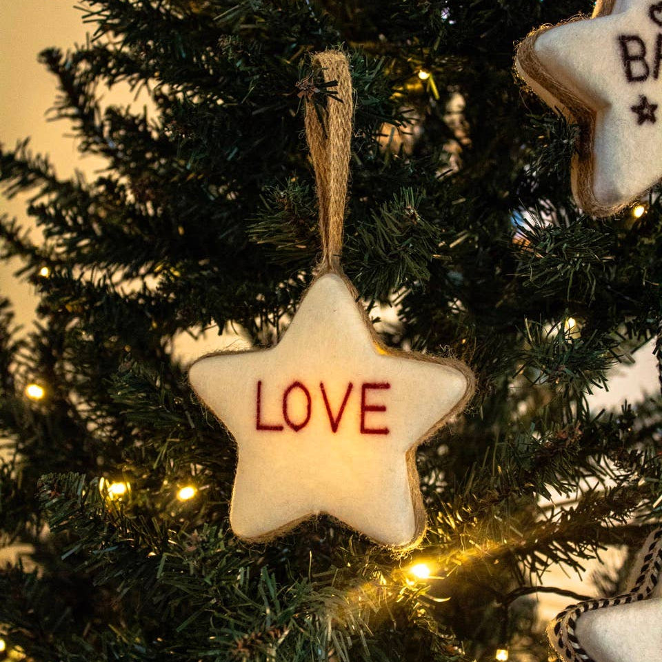 Star-shaped ornament with 'LOVE' text hanging on a decorated Christmas tree.