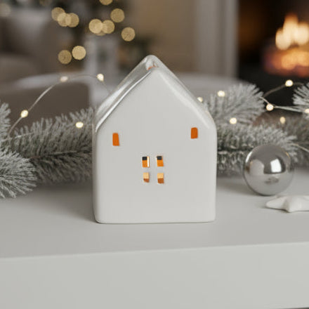 Decorative house tea light holder on a table with Christmas tree and fireplace in the background