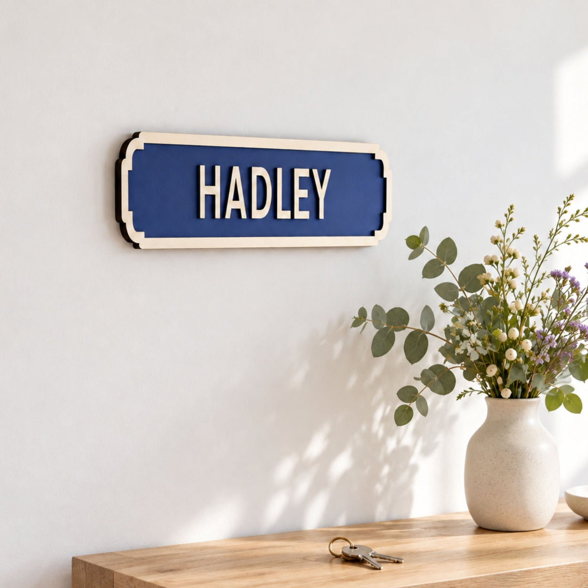 Blue personalised “Hadley” street-style sign with raised wooden lettering, displayed above an oak console with flowers.