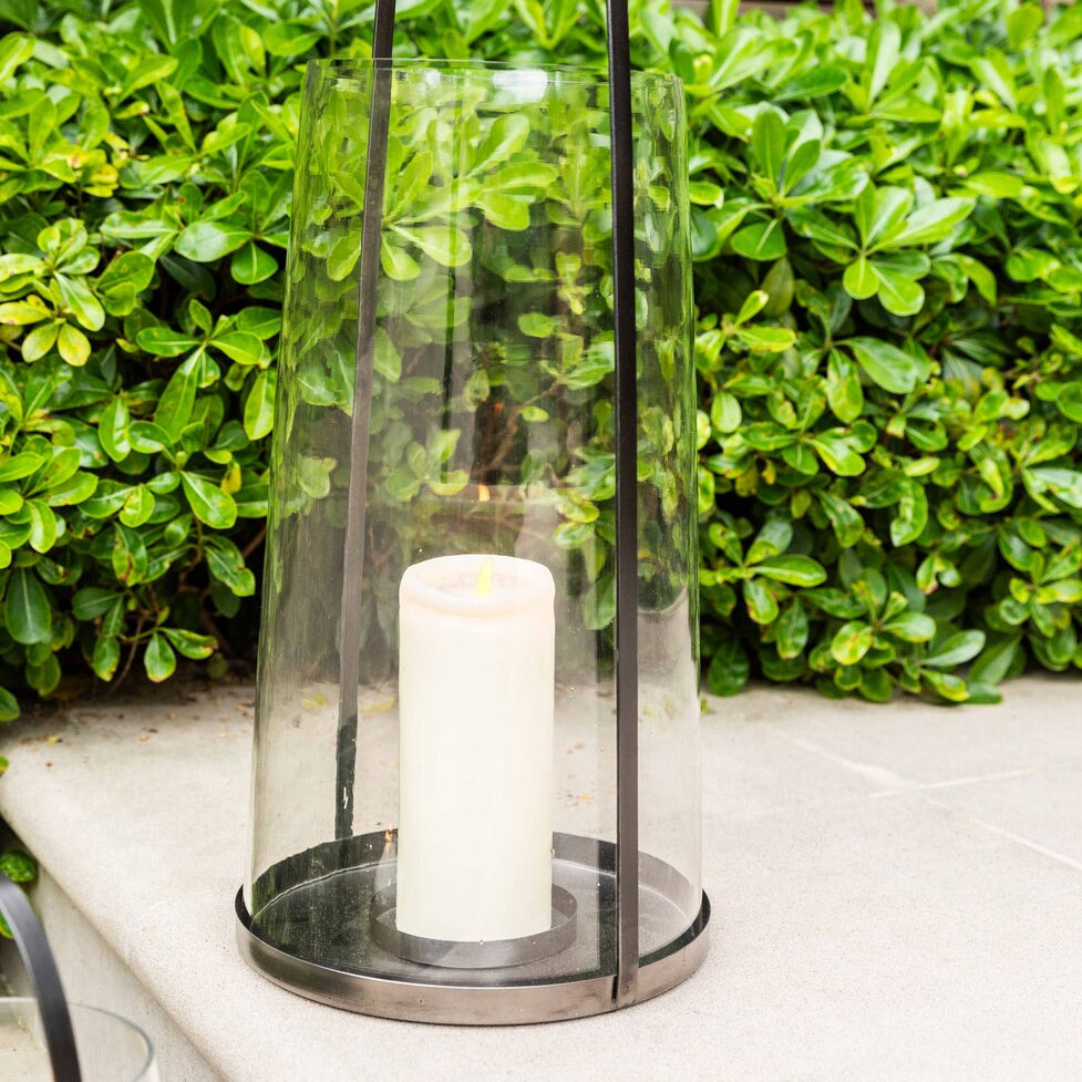 Glass lantern with a candle on a patio with greenery in the background