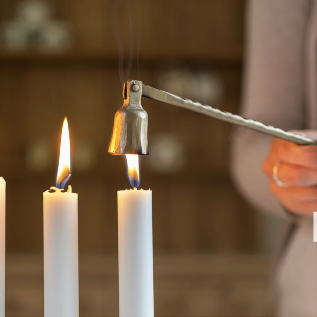 Candle snuffer being used to extinguish three candles with a blurred background