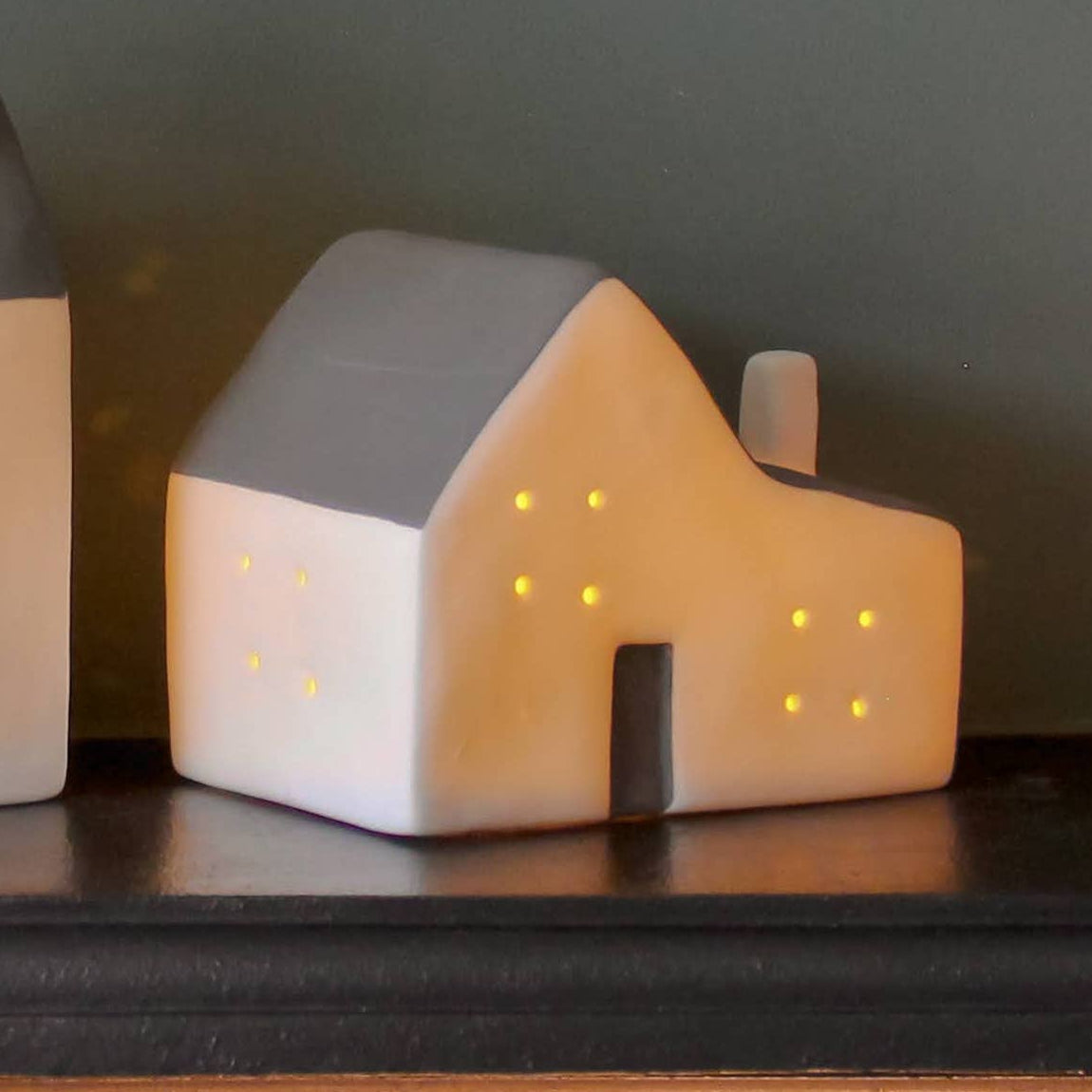  ceramic house-shaped lamps on a dark surface with a green plant and candle in the background.