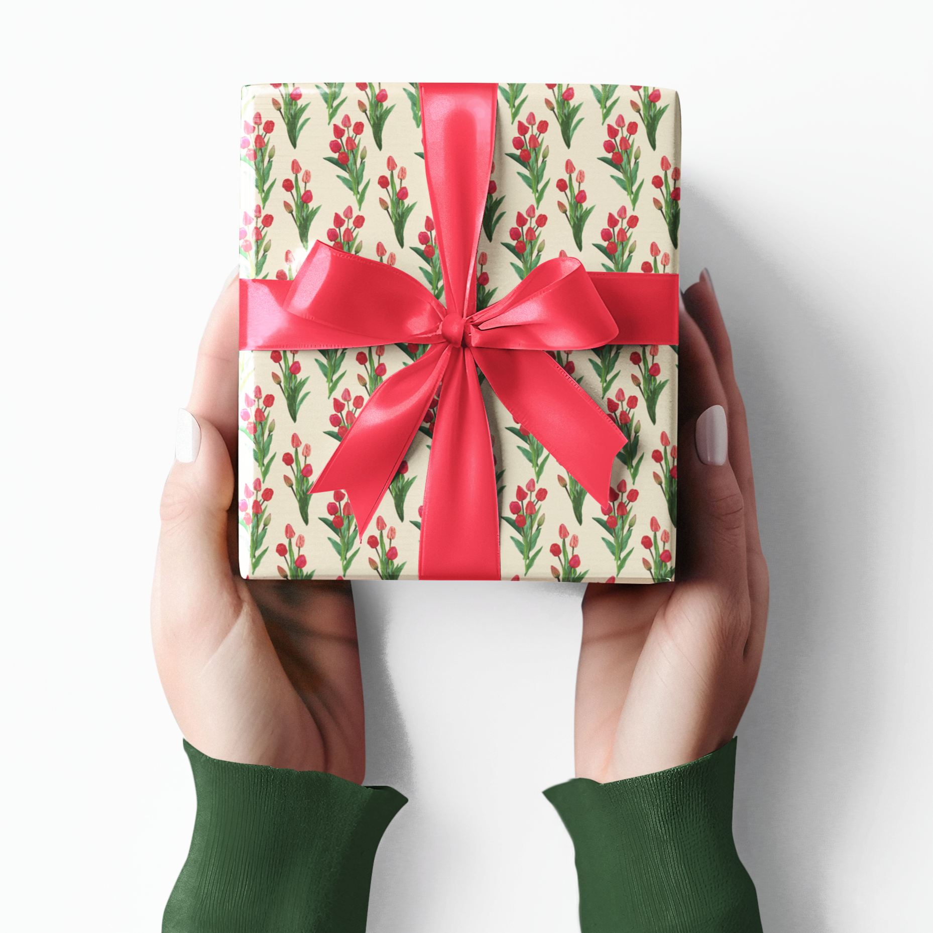 Gift box with floral tulip pattern and red ribbon held by hands wearing green sleeves on a white background