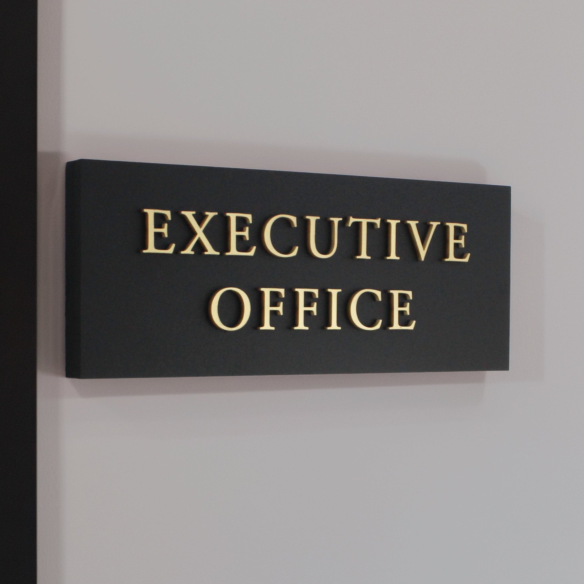 Black sign with raised gold wording shown in an office space