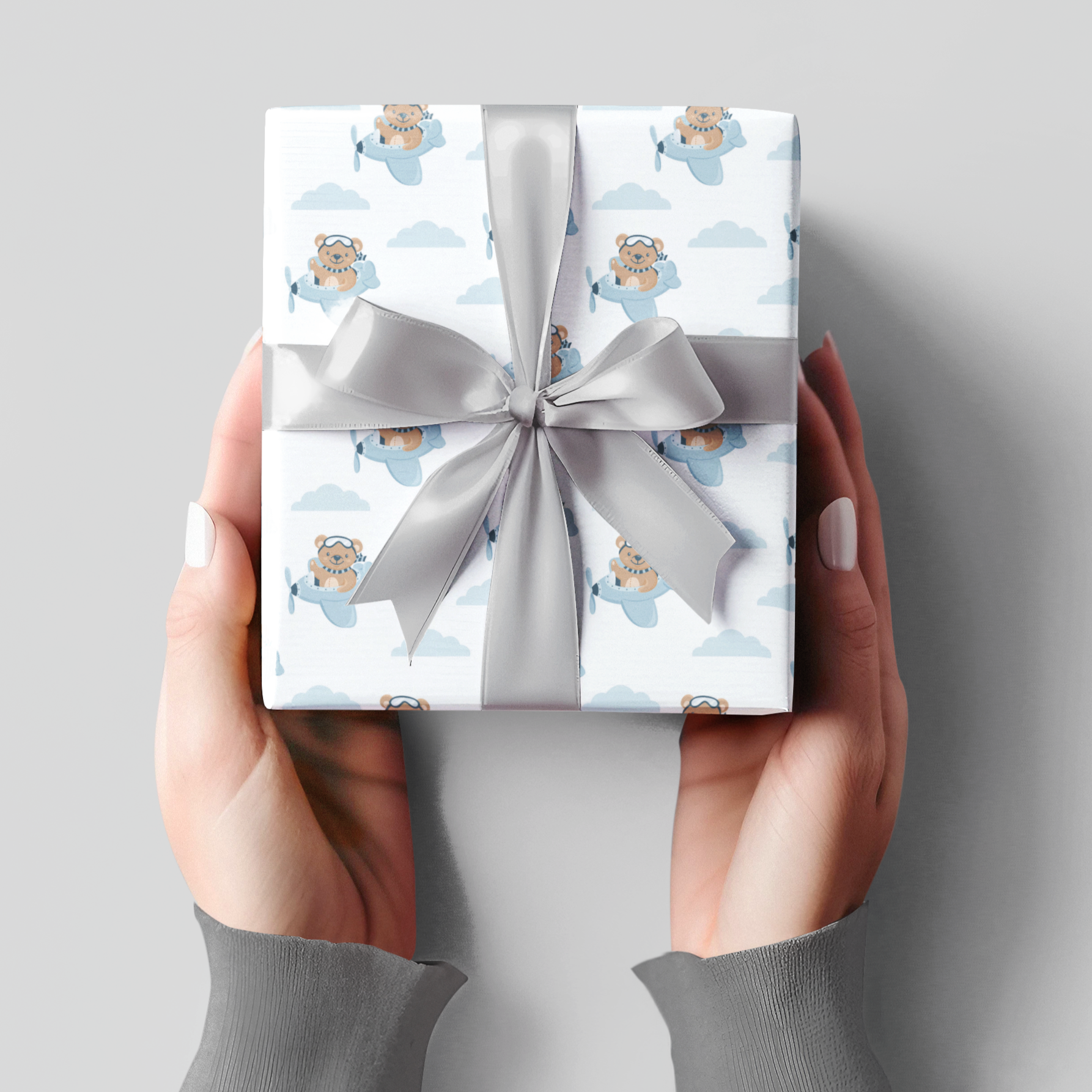Gift box with teddy bear pattern and silver ribbon held by hands against a gray background