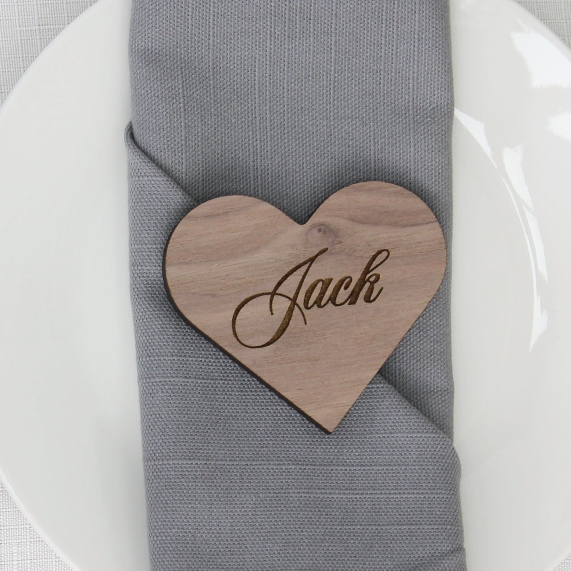 Napkin with a wooden heart-shaped name tag on a table setting with cutlery and a white plate.
