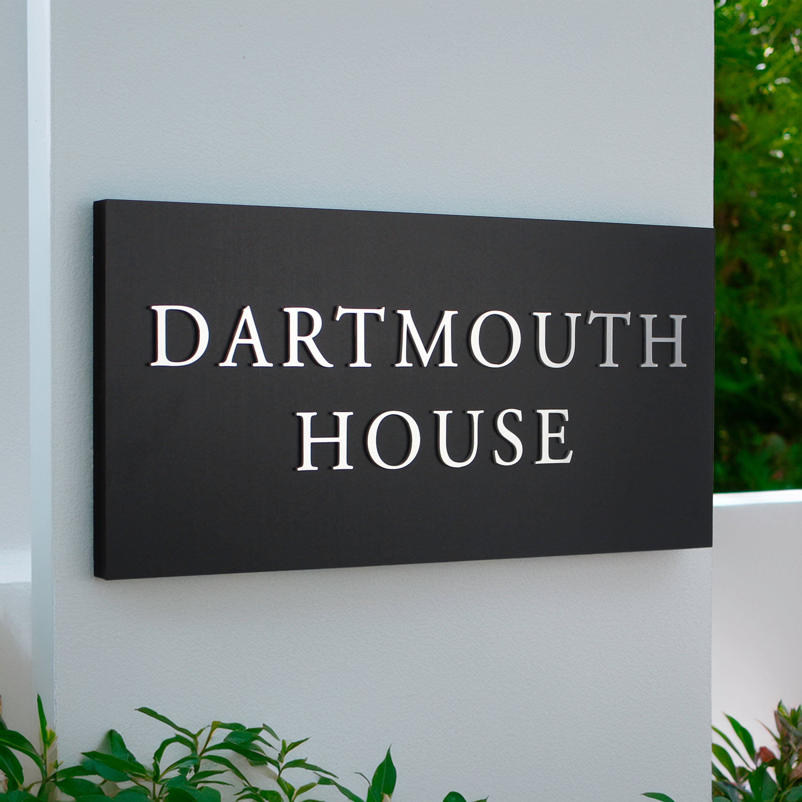large matte black house sign with raised silver design text over 2 lines