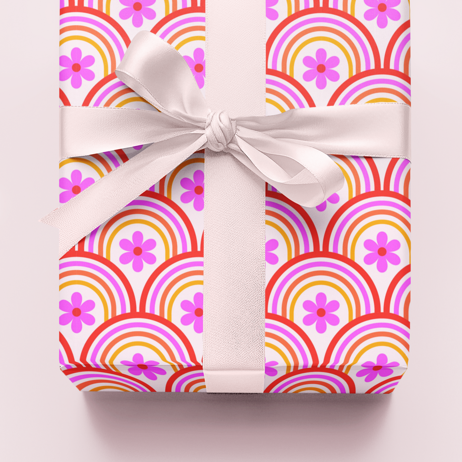 Gift wrap in colourful orange and pink retro  patterned paper with a white ribbon on a light pink background
