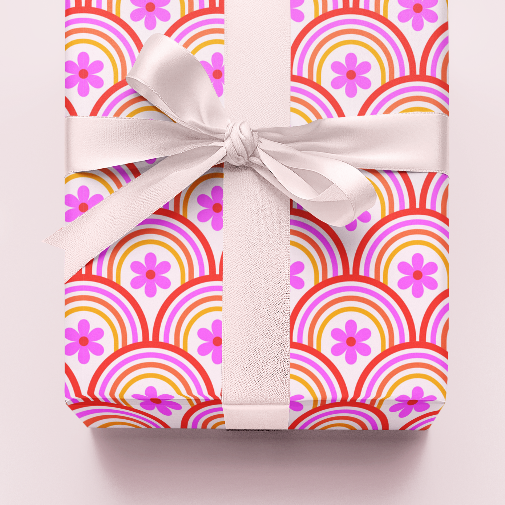 Gift wrap in colourful orange and pink retro  patterned paper with a white ribbon on a light pink background
