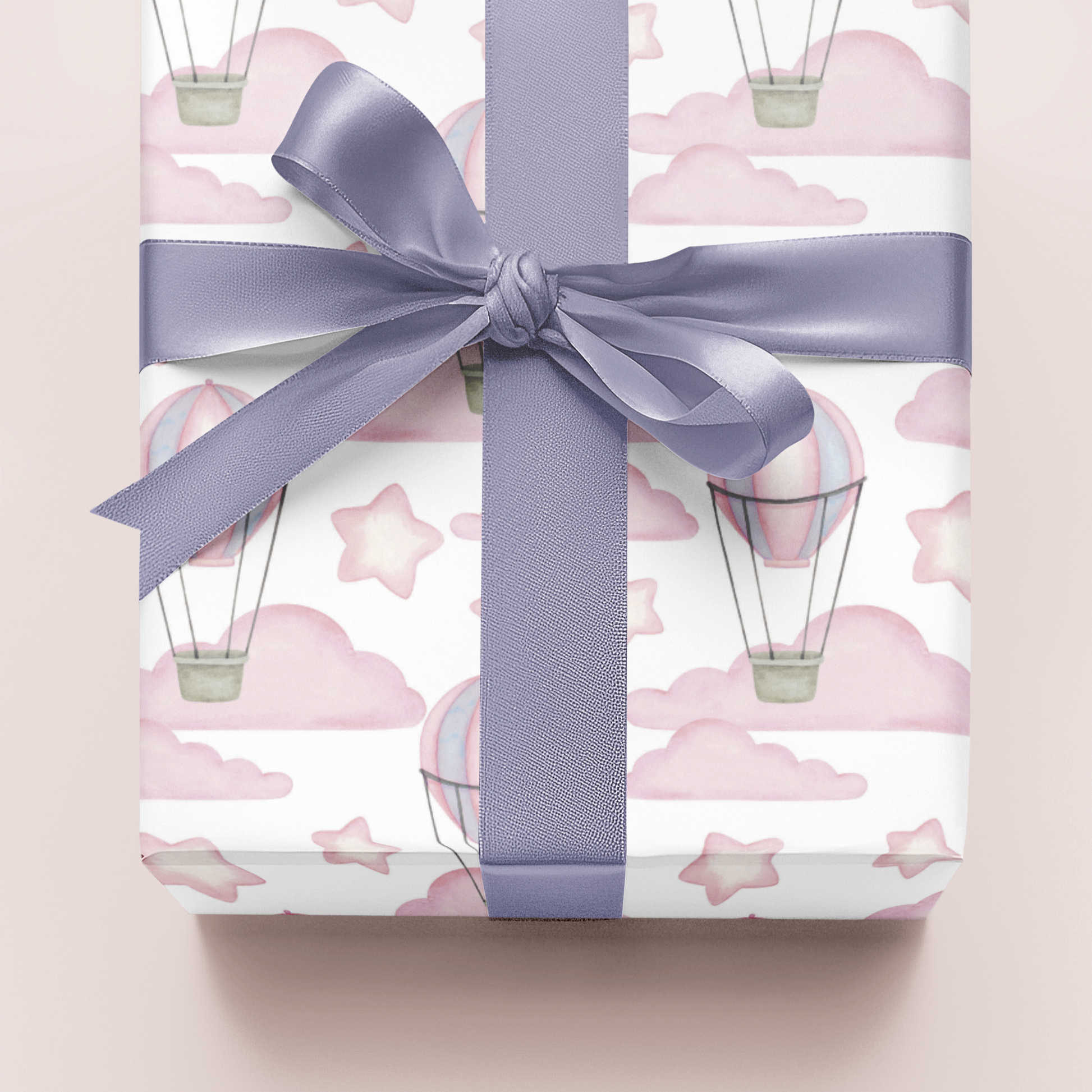 Gift wrapped in paper with hot air balloon design and a purple ribbon on a light pink background