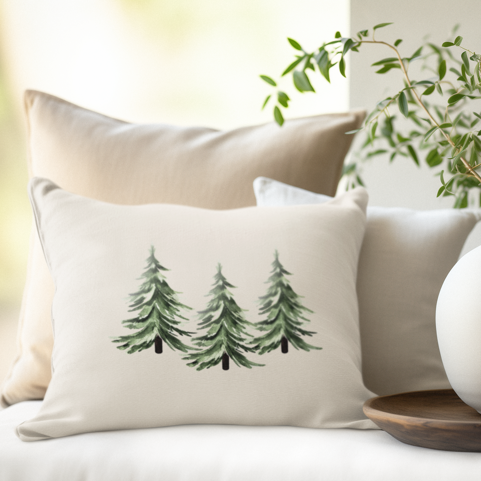 Decorative pillow with tree design on a couch next to a vase with greenery.