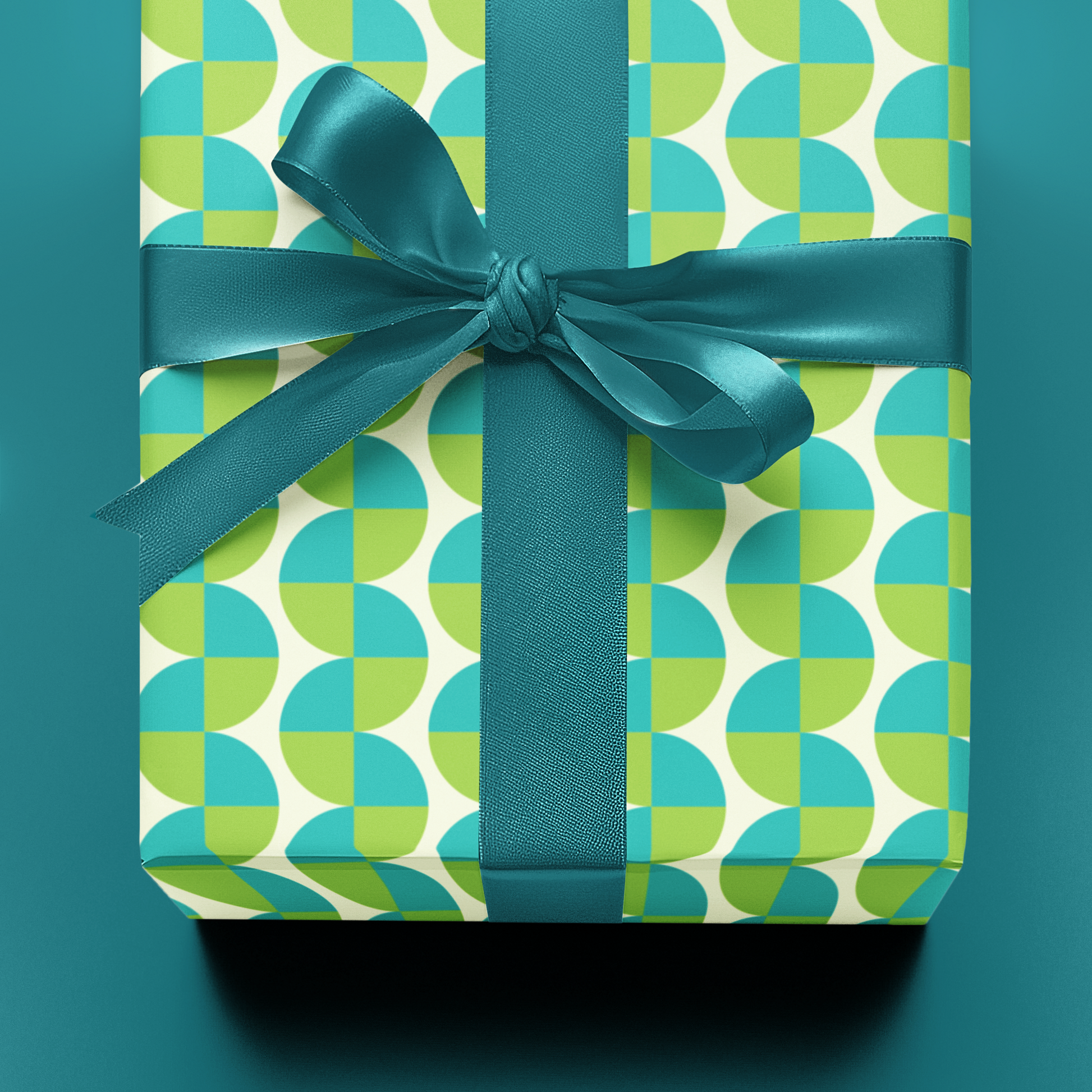 Gift box with green and blue patterned wrapping paper and a matching ribbon on a teal background
