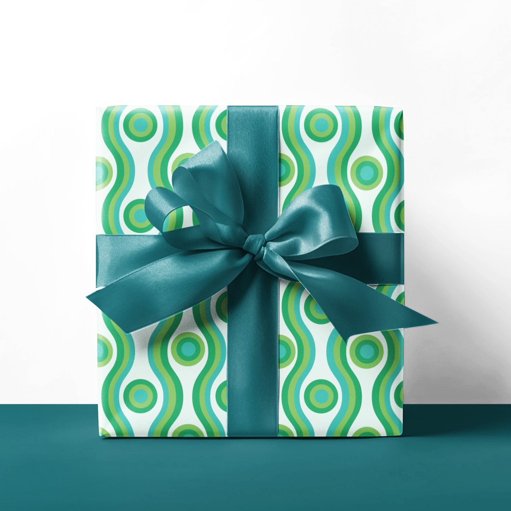 Gift box with green and white pattern and blue ribbon on a teal surface.