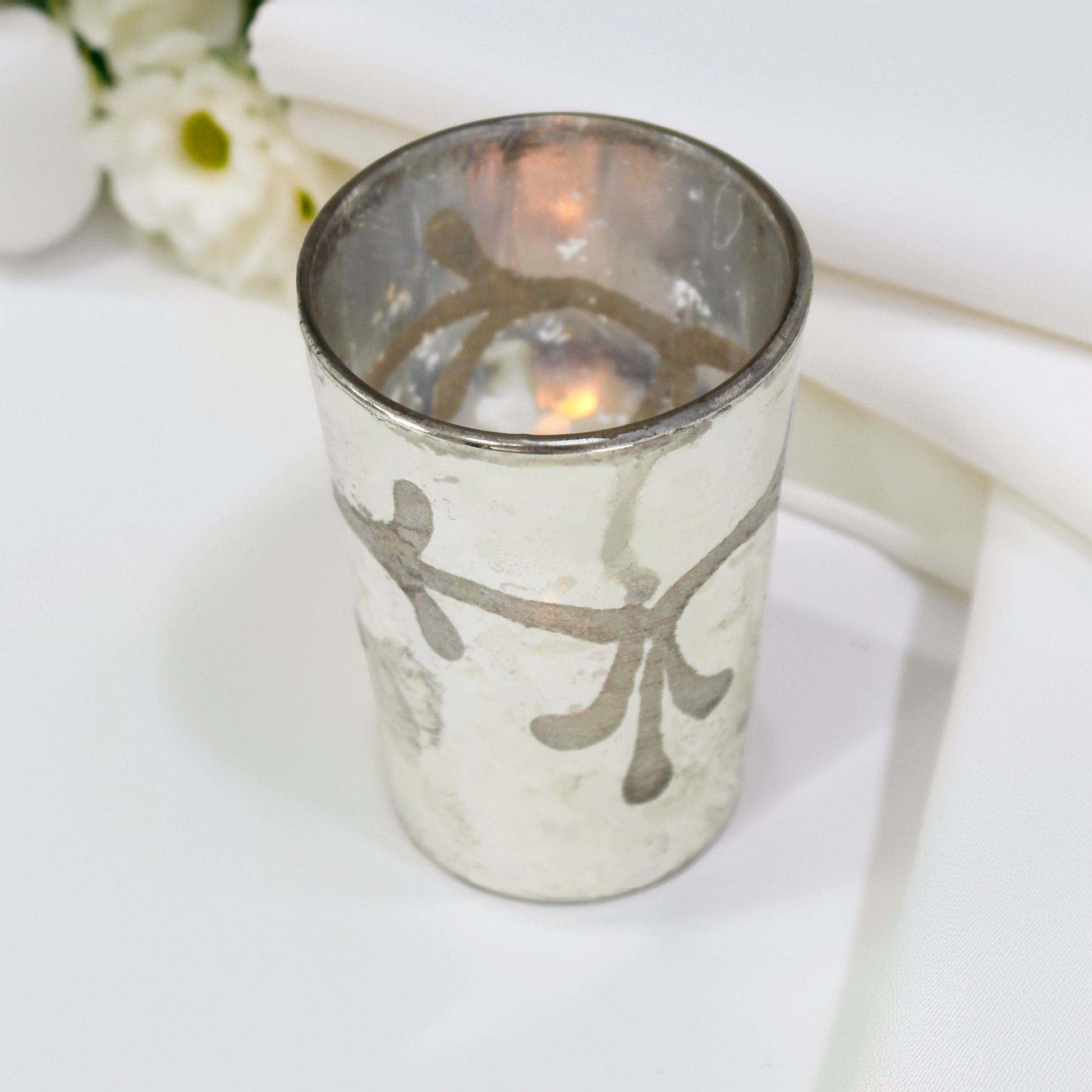 Silver candle holder with floral design on a white surface