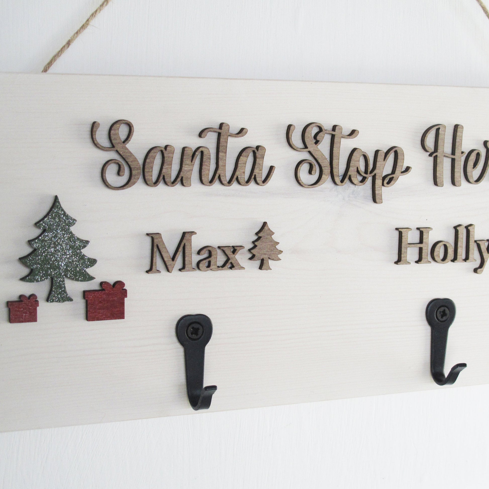 Decorative sign with 'Santa Stop Here' text and hooks on a white background