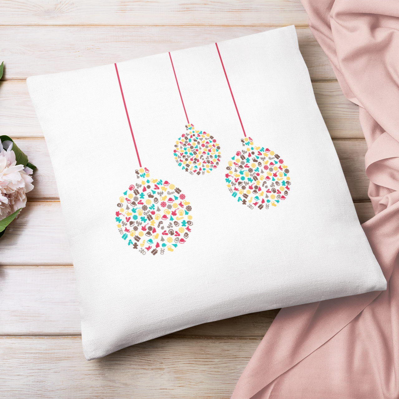 Decorative pillow with coloruful bauble design on a wooden surface with flowers and fabric.