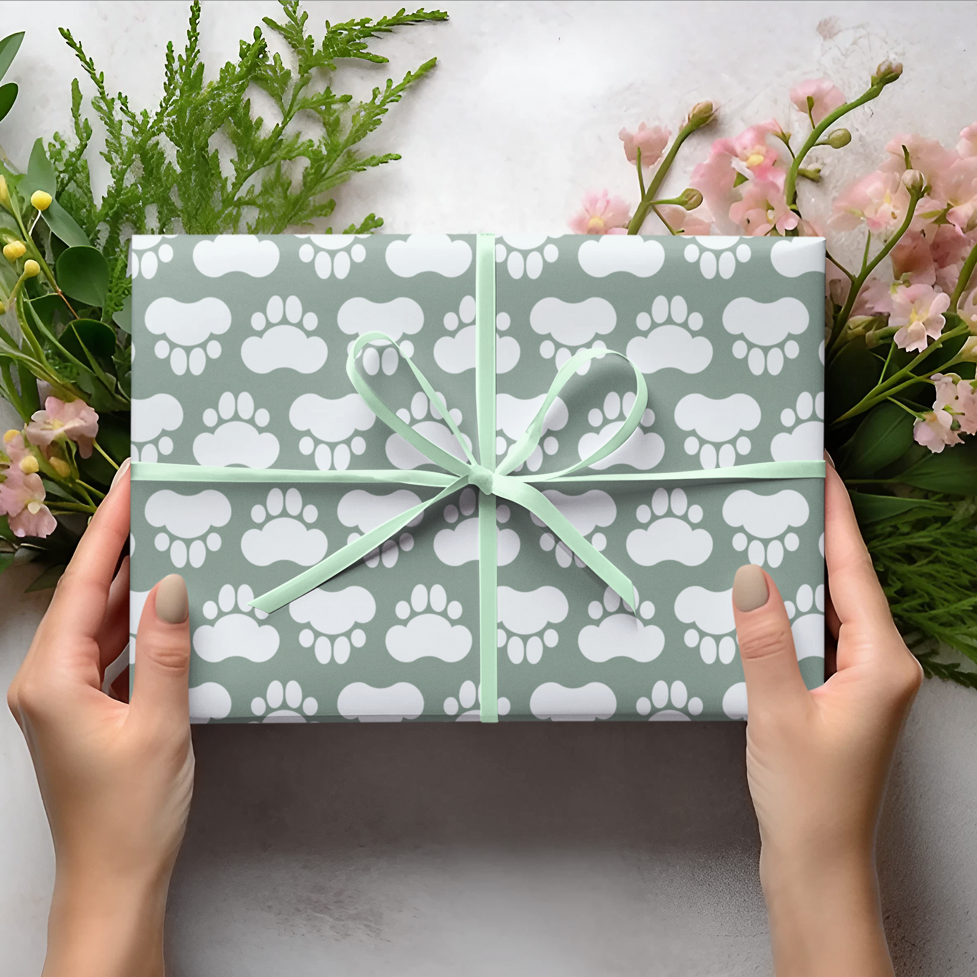 Gift box with paw print pattern held by hands on a light background with flowers and leaves.