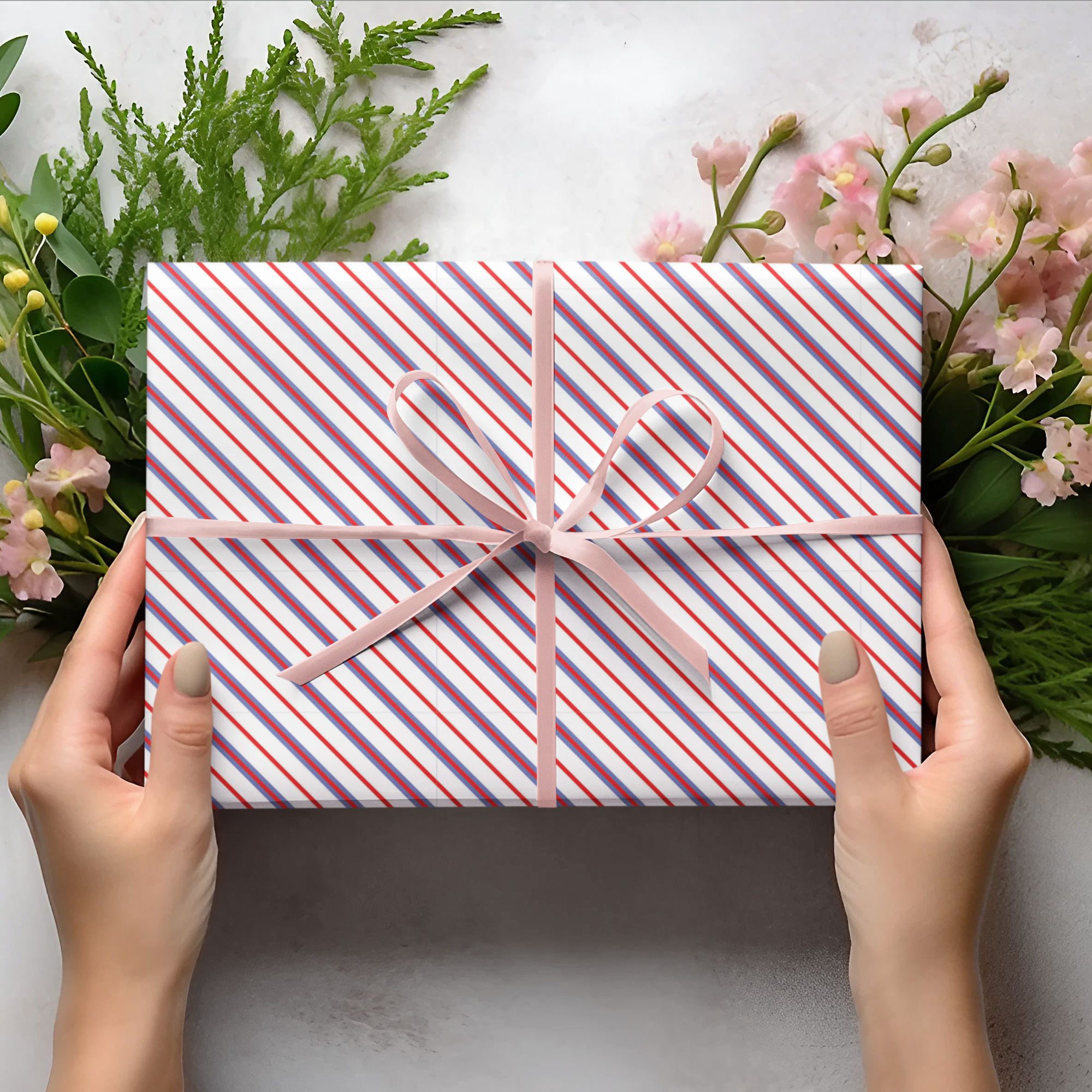 Person holding a striped gift box with floral and greenery arrangement on a light background