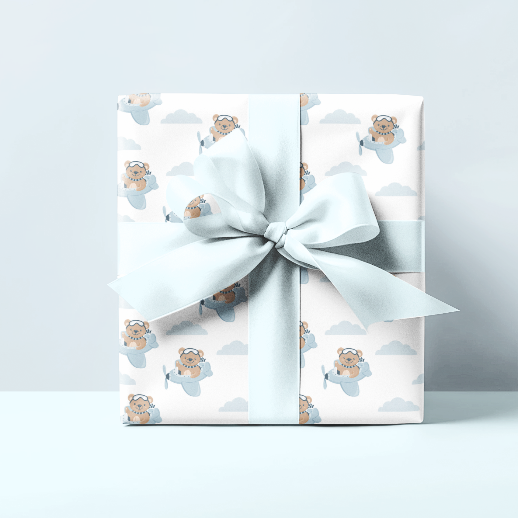 Gift wrap with a teddy bear and blue tones and  ribbon on a light grey background, perfect for small boy or newborn gifts