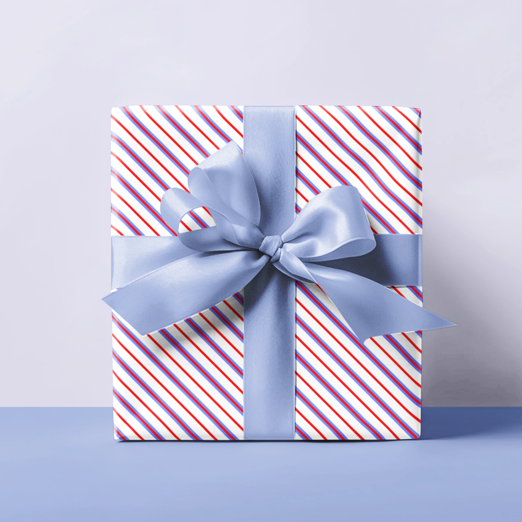 Gift wrap paper with red blue and white stripes and a blue bow on a light purple background